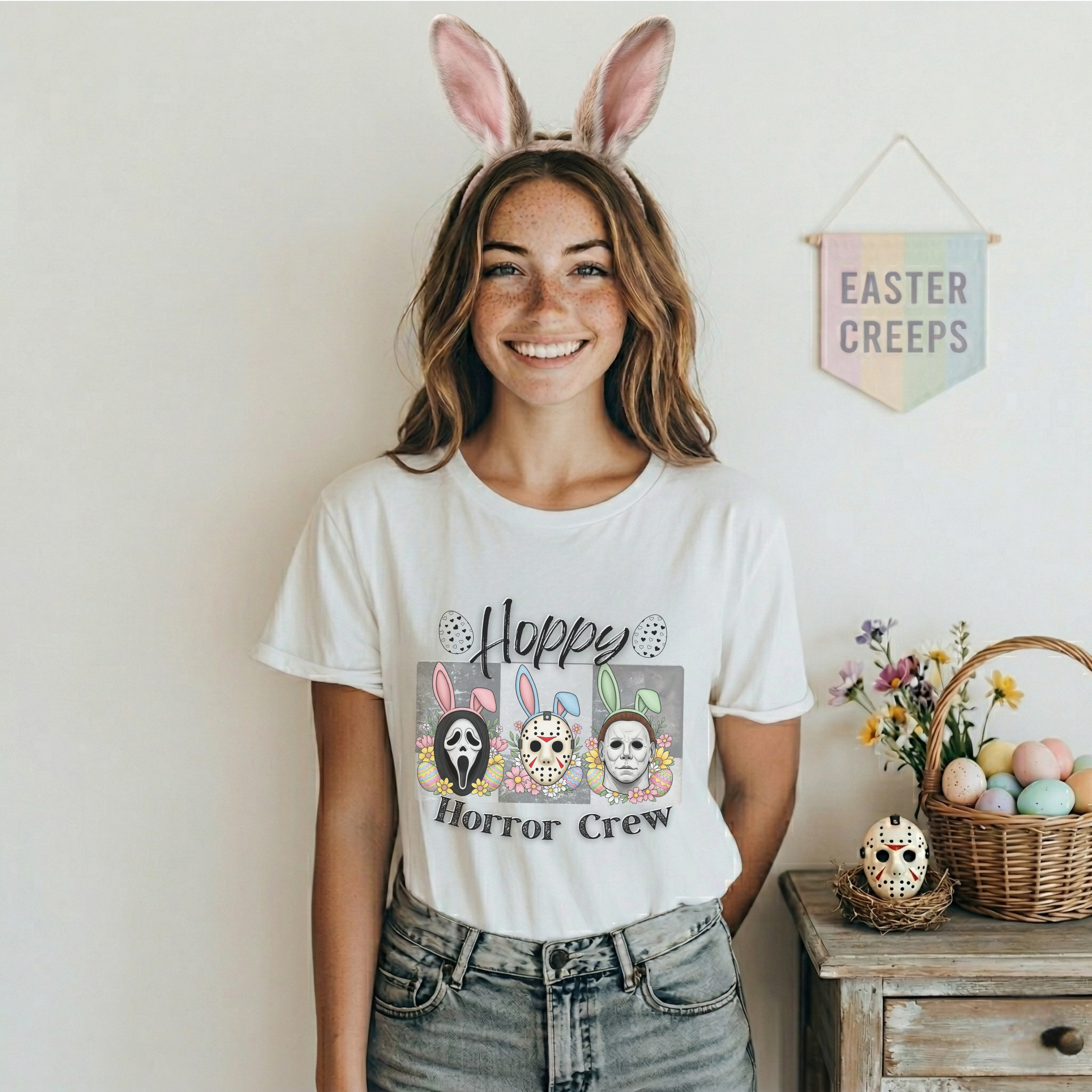 Person wearing a white t-shirt with a graphic design and bunny ears, standing in a room decorated for Easter.