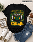 A black short-sleeve graphic T-shirt laid flat with jeans, white sneakers, a small sign, and a football around it on a light beige surface. The shirt reads "WARRIORS FOOTBALL" with a large football and letter "W" graphic in green, yellow, and white.