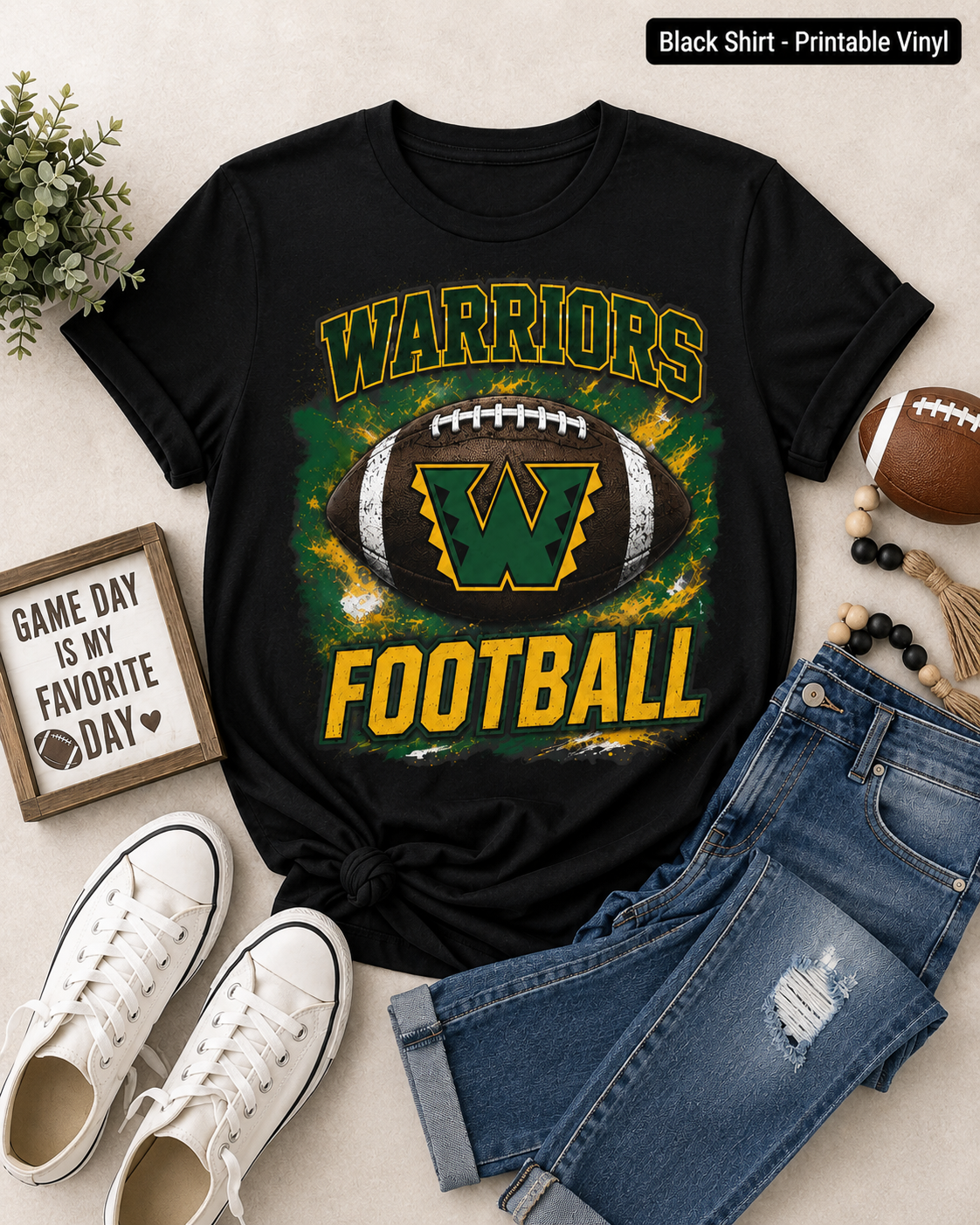 A black short-sleeve graphic T-shirt laid flat with jeans, white sneakers, a small sign, and a football around it on a light beige surface. The shirt reads "WARRIORS FOOTBALL" with a large football and letter "W" graphic in green, yellow, and white.