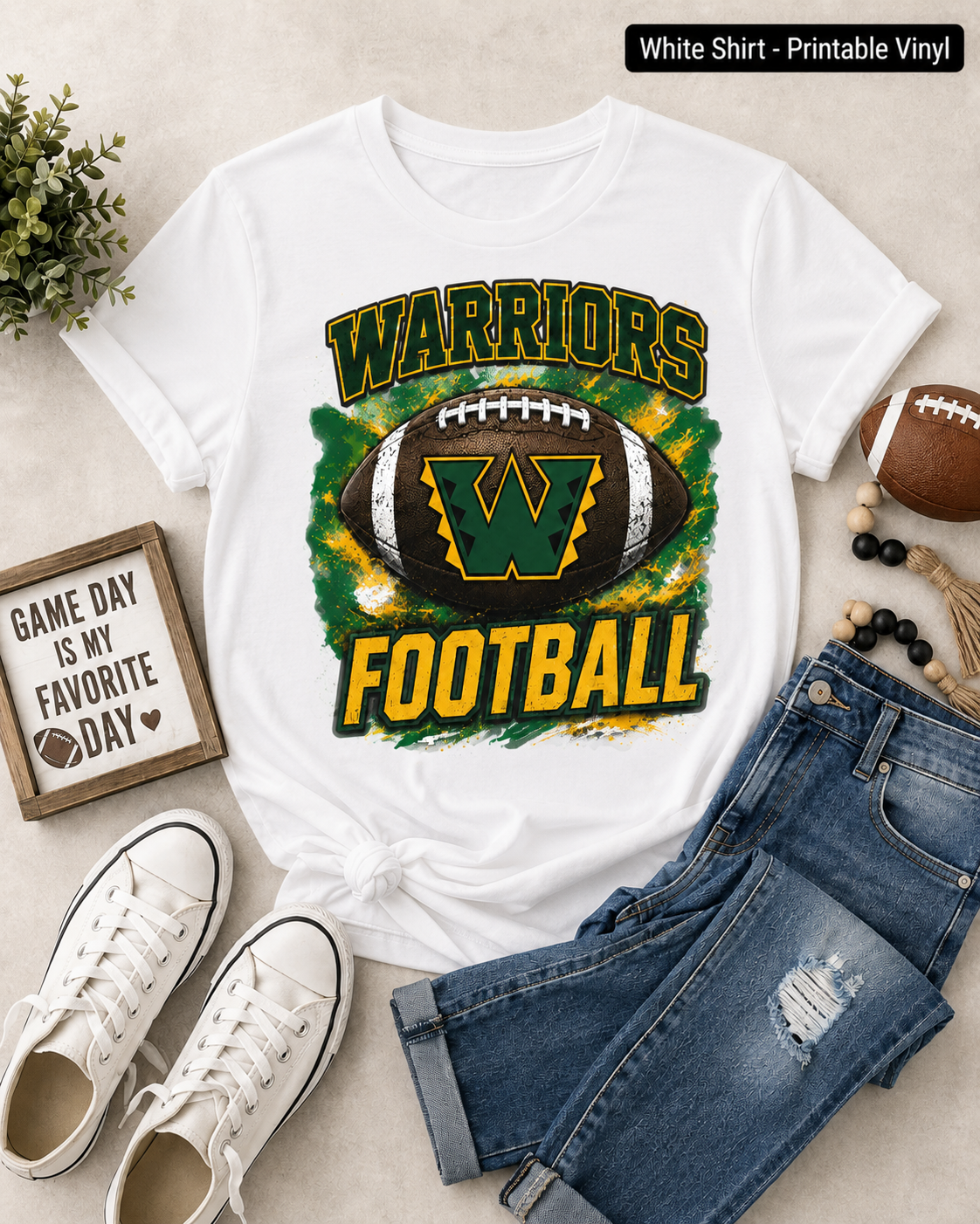 A white graphic t-shirt featuring a 'Warriors Football' design with a green and yellow football, styled in a flat-lay arrangement with blue jeans, white sneakers, a small decorative sign, and a football on a light beige background.