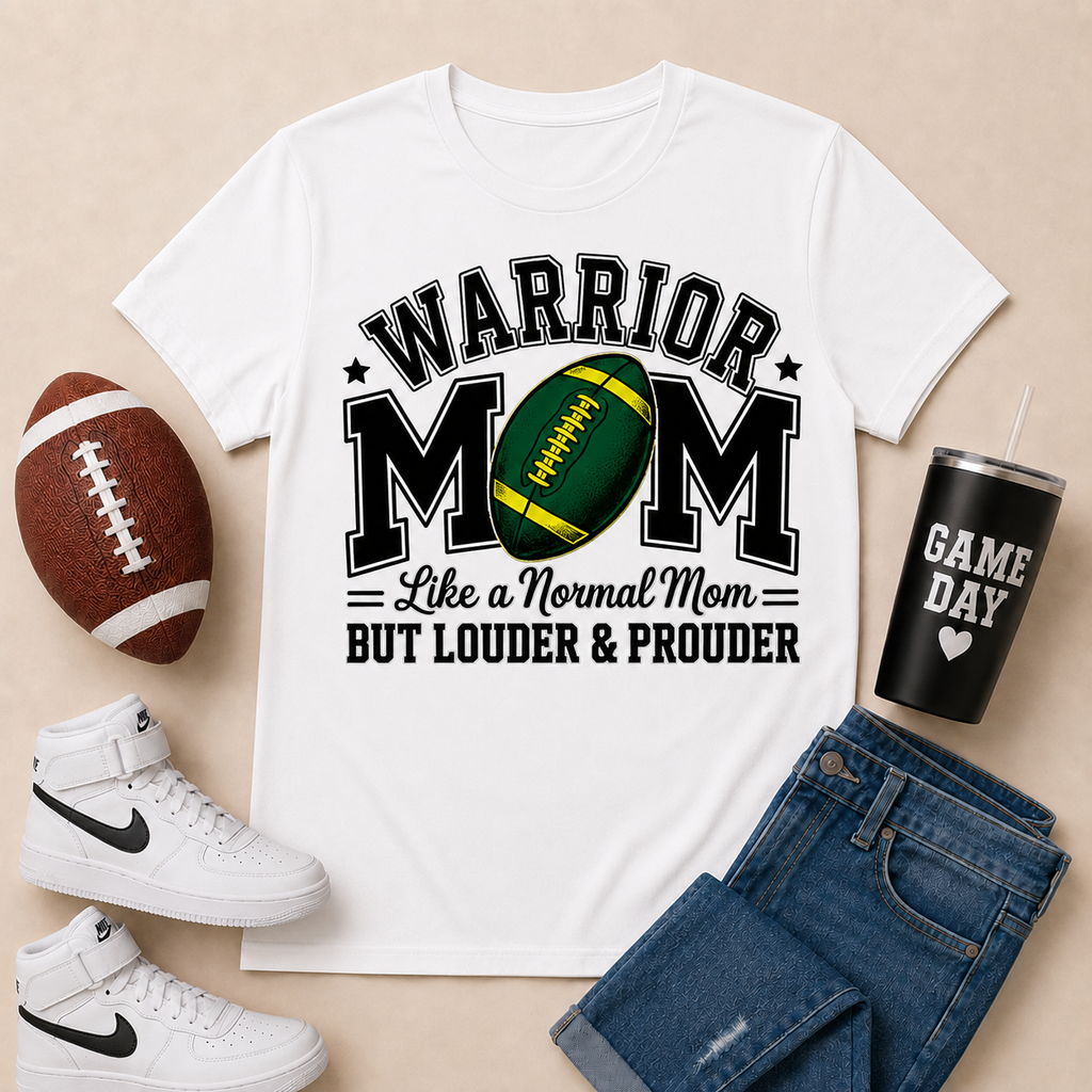 A white graphic T-shirt laid flat on a beige background, surrounded by a brown football, white high-top sneakers, blue jeans, and a black tumbler with the words 'GAME DAY'. The shirt reads 'WARRIOR MOM Like a Normal Mom BUT LOUDER & PROUDER' with a green and yellow football graphic.